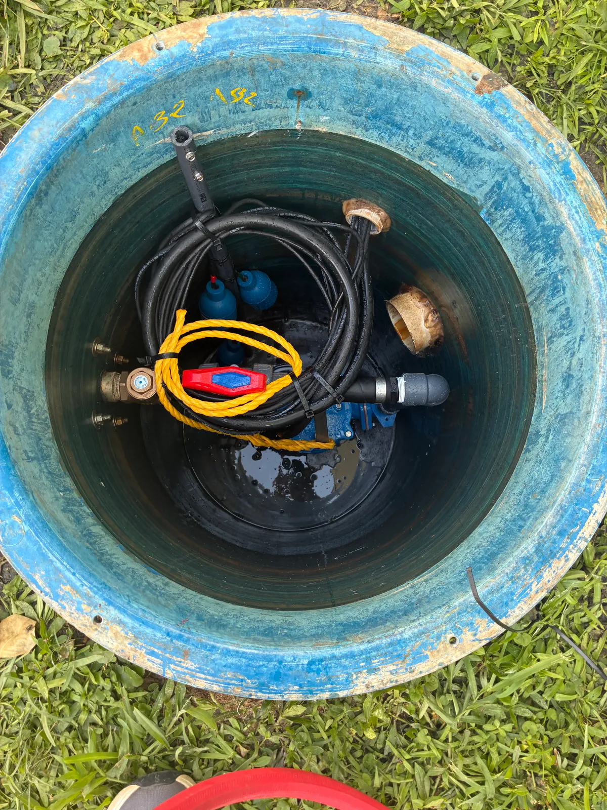 A grinder pump station opened up in its basin, showing the pump, float switch, discharge piping, and lift rope