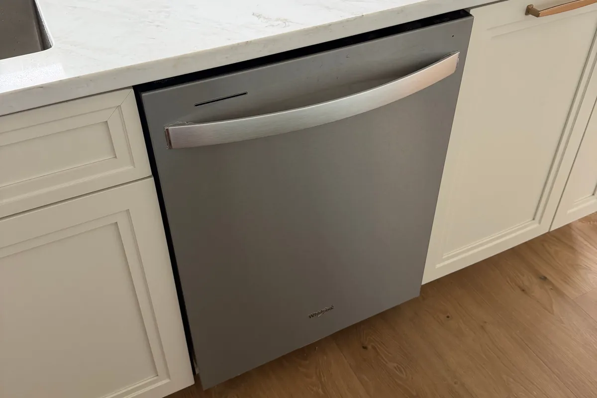 A stainless dishwasher hooked up and set into its cabinet opening under a quartz countertop, sitting square against the adjoining cabinet faces