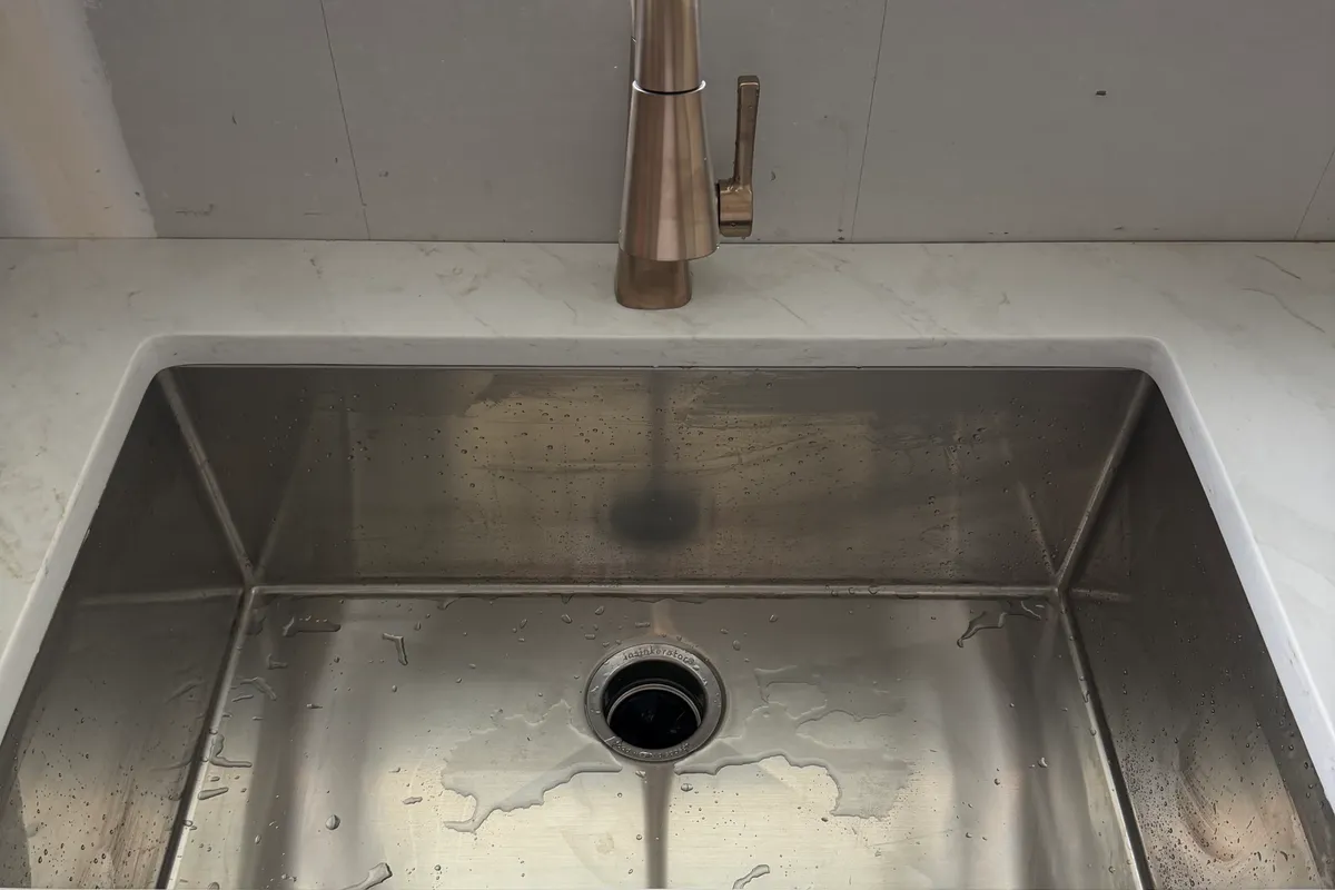 A stainless undermount kitchen sink and brushed pull-down faucet set in a quartz countertop, basin still wet from the first test run